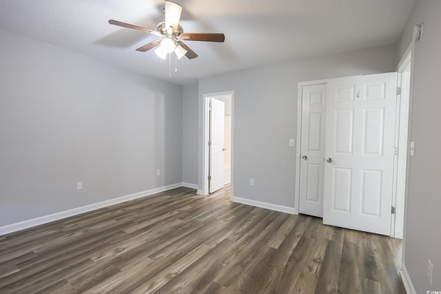 unfurnished bedroom featuring dark wood-type flooring, ensuite bath, baseboards, and a ceiling fan