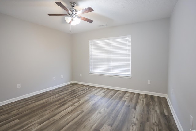 spare room with dark wood-style floors, ceiling fan, visible vents, and baseboards