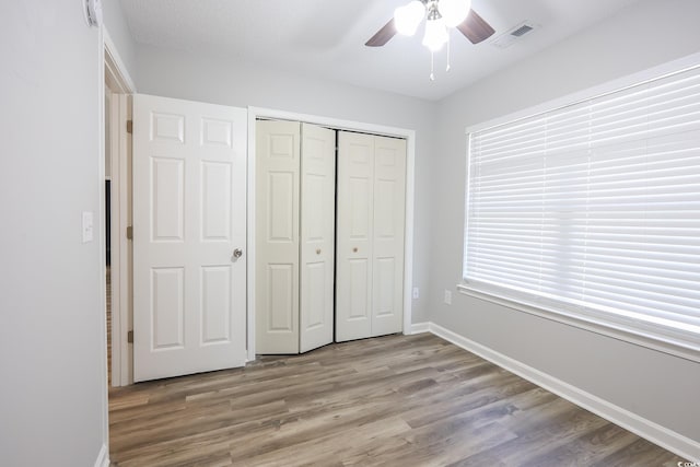 unfurnished bedroom featuring a closet, visible vents, ceiling fan, wood finished floors, and baseboards