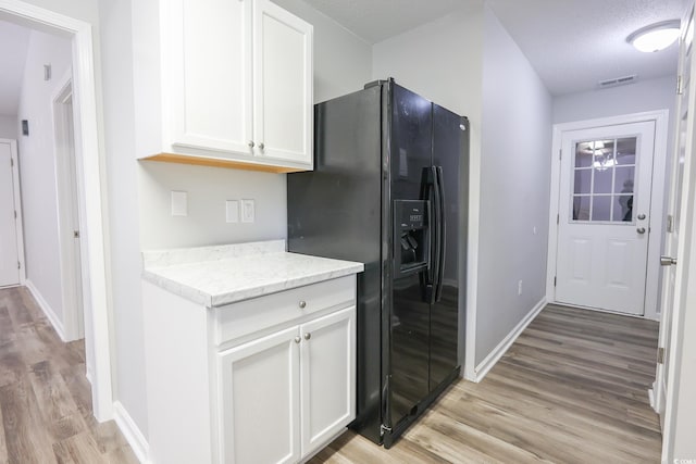 kitchen featuring light wood-style flooring, black fridge with ice dispenser, visible vents, baseboards, and white cabinets