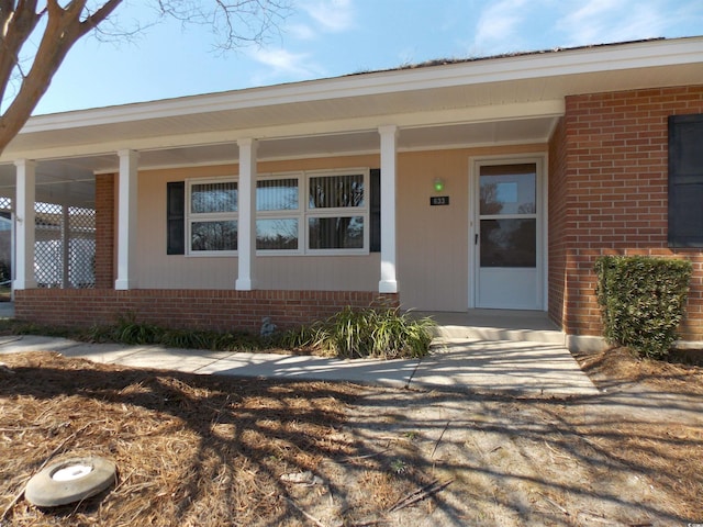 entrance to property with a porch and brick siding