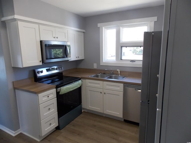 kitchen featuring wood finished floors, a sink, white cabinetry, light countertops, and appliances with stainless steel finishes