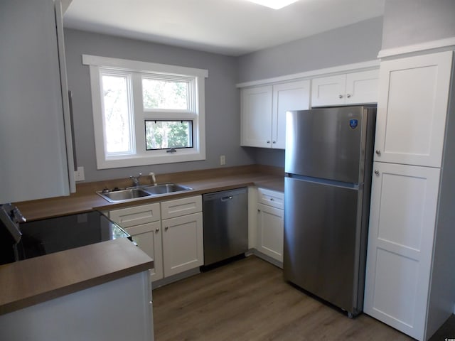 kitchen featuring appliances with stainless steel finishes, white cabinets, a sink, and light wood-style flooring