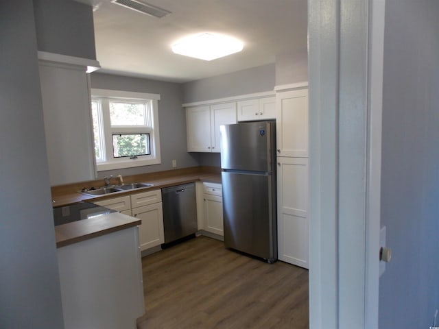 kitchen with stainless steel appliances, wood finished floors, a sink, visible vents, and white cabinetry