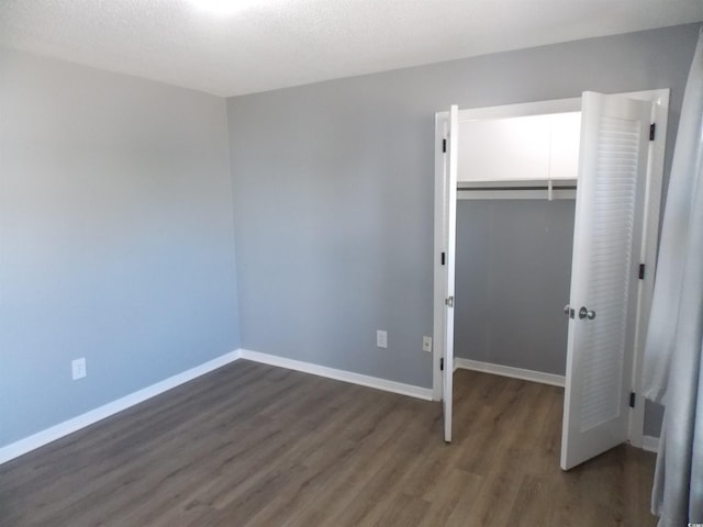 unfurnished bedroom featuring a walk in closet, a closet, baseboards, and wood finished floors