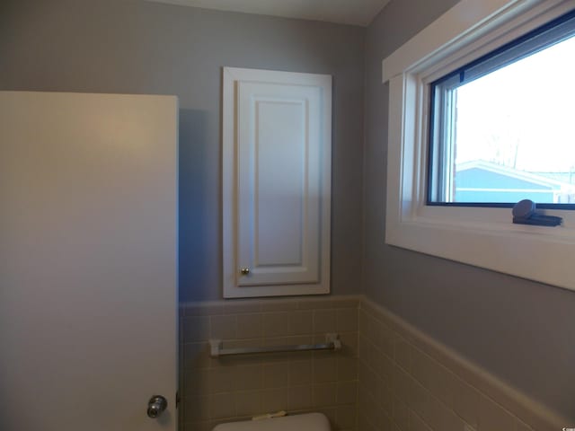 half bath featuring a wainscoted wall, toilet, and tile walls