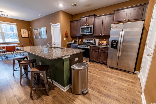 kitchen with a breakfast bar area, dark brown cabinetry, stainless steel appliances, a sink, and light wood finished floors