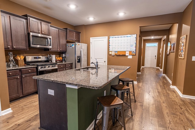 kitchen featuring a breakfast bar, stainless steel appliances, light wood-style flooring, a sink, and an island with sink