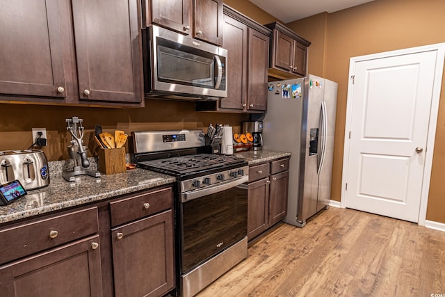 kitchen with baseboards, dark stone counters, stainless steel appliances, dark brown cabinets, and light wood-type flooring