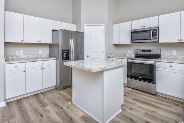 kitchen featuring a kitchen island, stainless steel appliances, a towering ceiling, white cabinetry, and light wood-type flooring