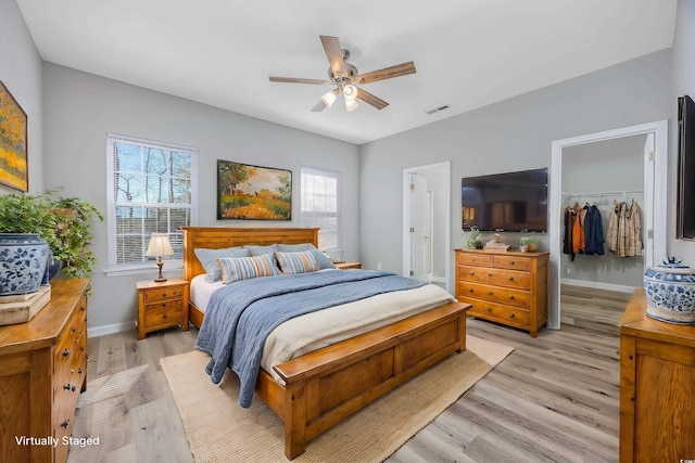 bedroom featuring a walk in closet, baseboards, ceiling fan, light wood-type flooring, and a closet