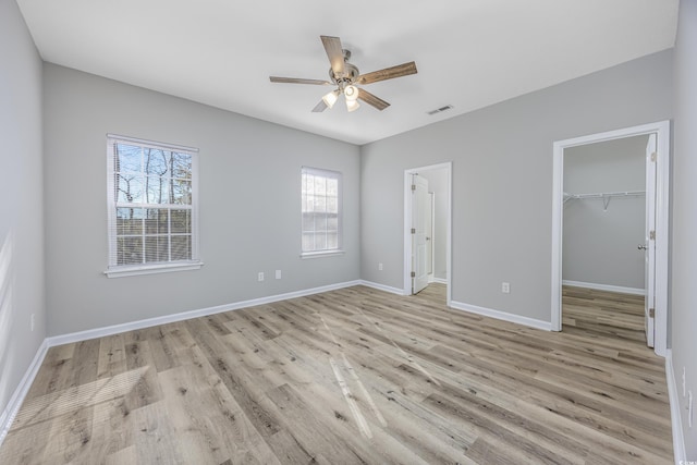 unfurnished bedroom featuring light wood-style floors, a closet, a walk in closet, and baseboards