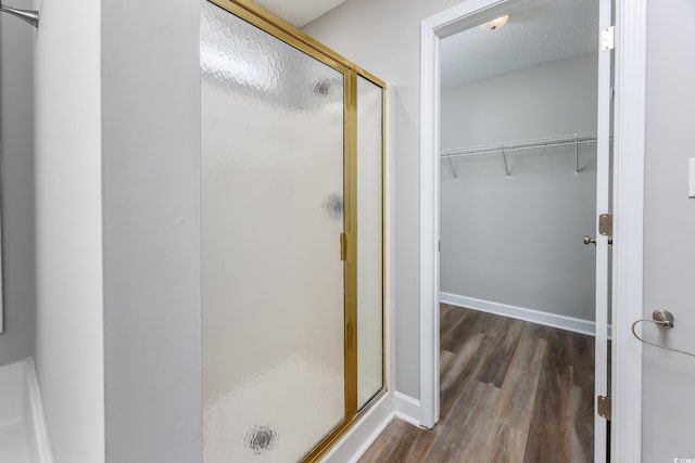 bathroom with a walk in closet, a shower stall, wood finished floors, and baseboards