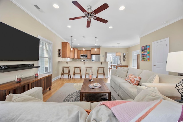 living area with light wood finished floors, recessed lighting, visible vents, ornamental molding, and baseboards