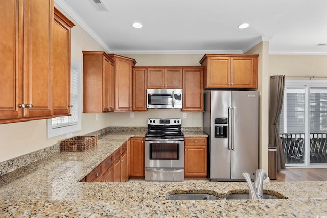 kitchen featuring stainless steel appliances, light stone counters, brown cabinetry, and a sink