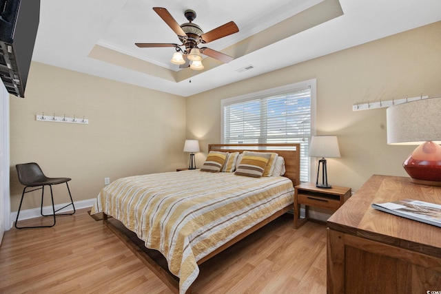 bedroom with a tray ceiling, visible vents, light wood-style floors, ornamental molding, and baseboards