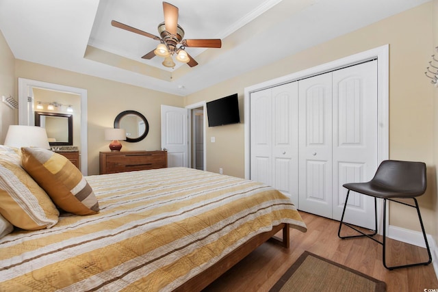 bedroom with wood finished floors, a ceiling fan, baseboards, a closet, and a raised ceiling