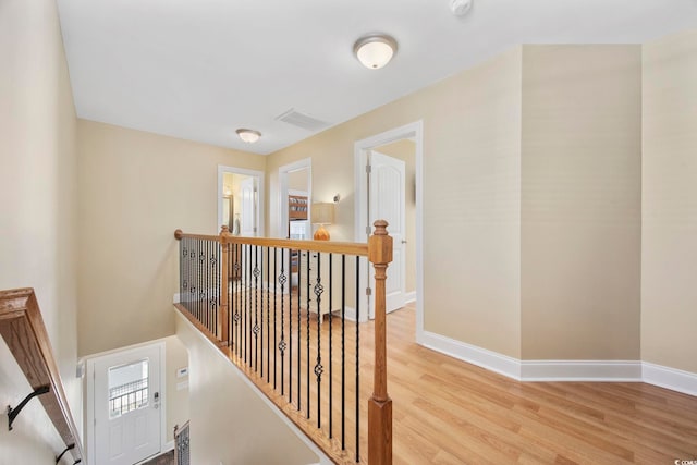 corridor with baseboards, visible vents, an upstairs landing, and wood finished floors