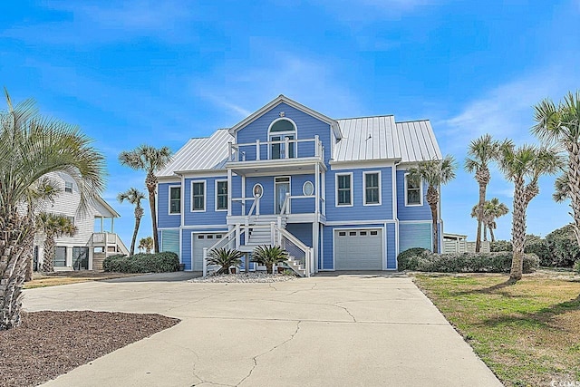 coastal inspired home with driveway, a balcony, metal roof, an attached garage, and stairs