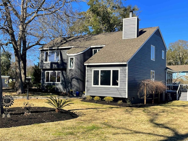 back of house featuring a lawn, a chimney, and roof with shingles