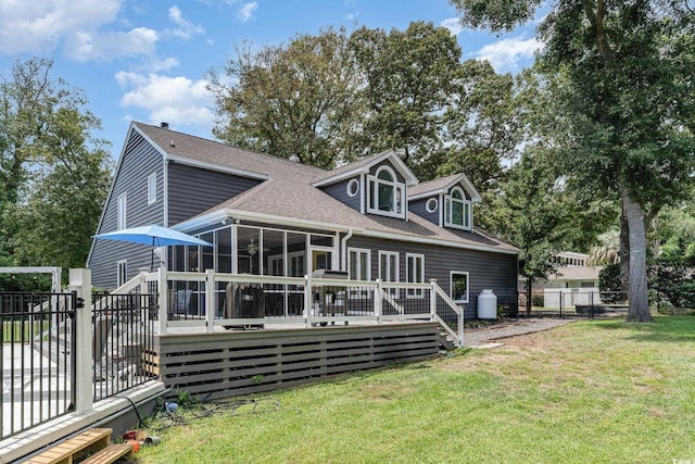 rear view of property featuring fence, roof with shingles, a wooden deck, a yard, and a sunroom