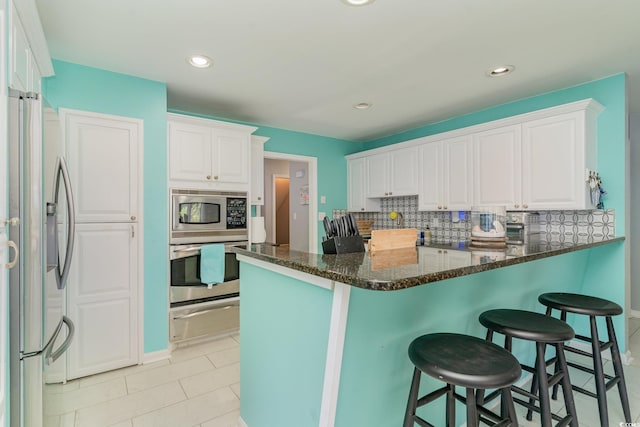 kitchen with a warming drawer, decorative backsplash, white cabinets, appliances with stainless steel finishes, and a kitchen breakfast bar