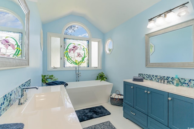 bathroom featuring a soaking tub, vaulted ceiling, two vanities, and a sink