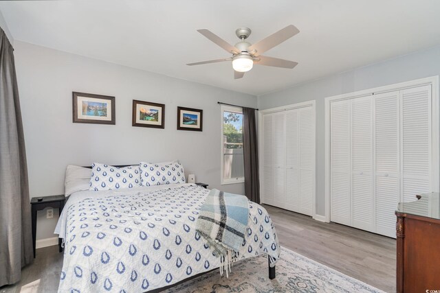 bedroom featuring wood finished floors, baseboards, two closets, and ceiling fan