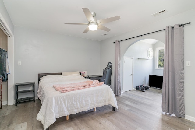 bedroom with wood finished floors, visible vents, arched walkways, and ceiling fan