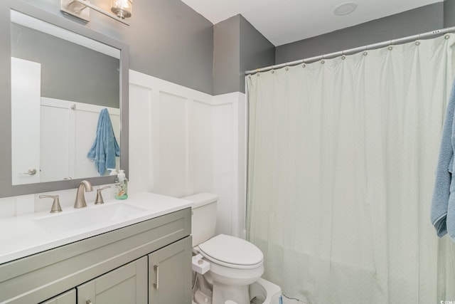 full bathroom with curtained shower, a wainscoted wall, toilet, a decorative wall, and vanity