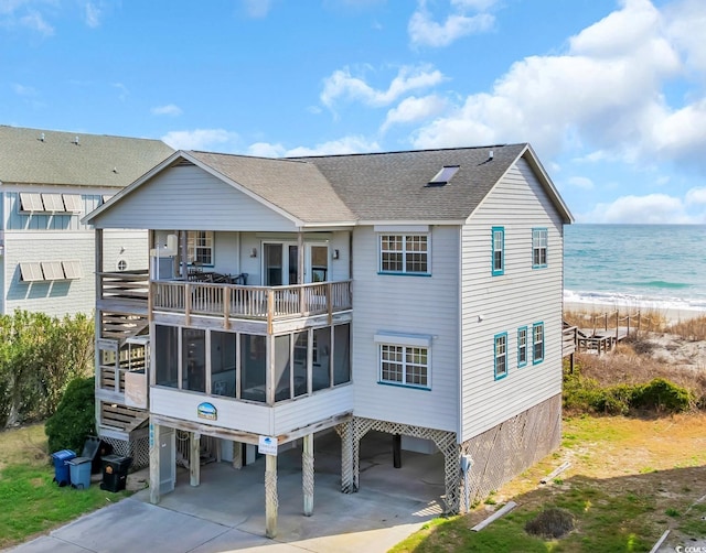 back of house featuring roof with shingles, a beach view, a water view, a sunroom, and a carport