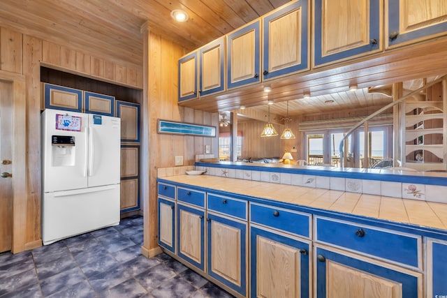 kitchen with white fridge with ice dispenser, wooden ceiling, tile counters, and wooden walls