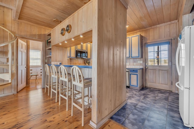 kitchen featuring stainless steel microwave, wooden ceiling, freestanding refrigerator, and wooden walls