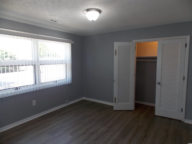 unfurnished bedroom with a closet, visible vents, dark wood-type flooring, a textured ceiling, and baseboards