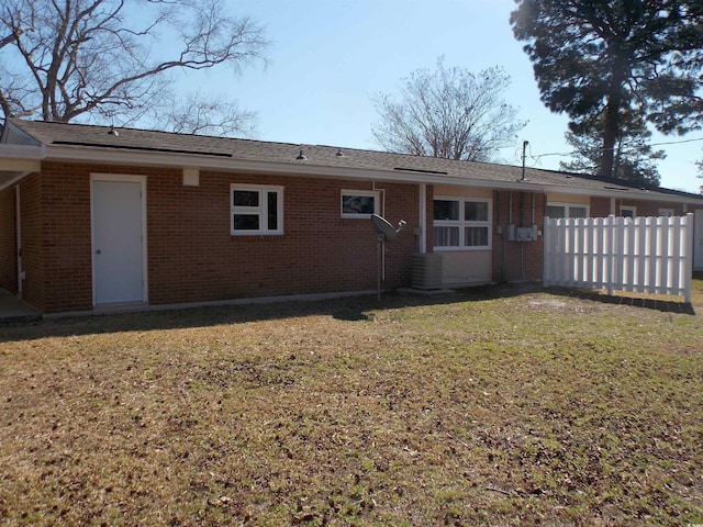 back of house with brick siding, fence, central AC, and a lawn