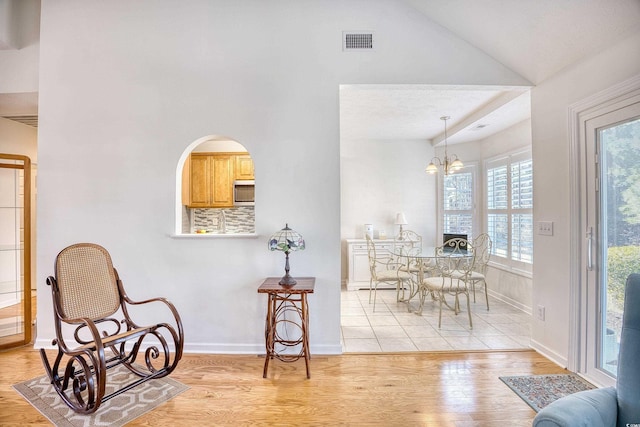 dining space with baseboards, visible vents, vaulted ceiling, a notable chandelier, and light wood-type flooring