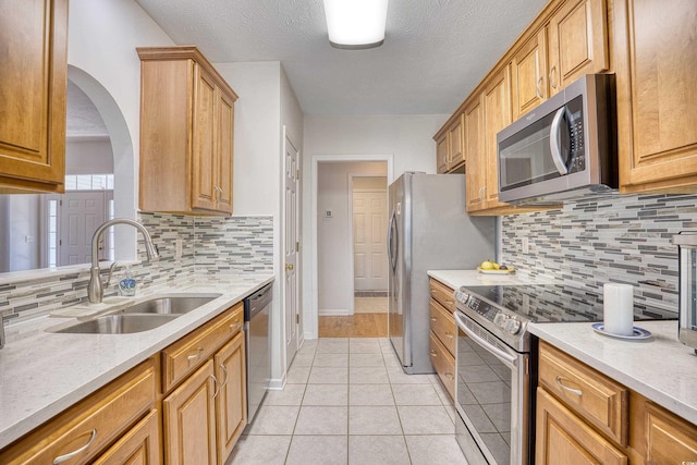 kitchen with light tile patterned floors, light stone countertops, a sink, decorative backsplash, and stainless steel appliances