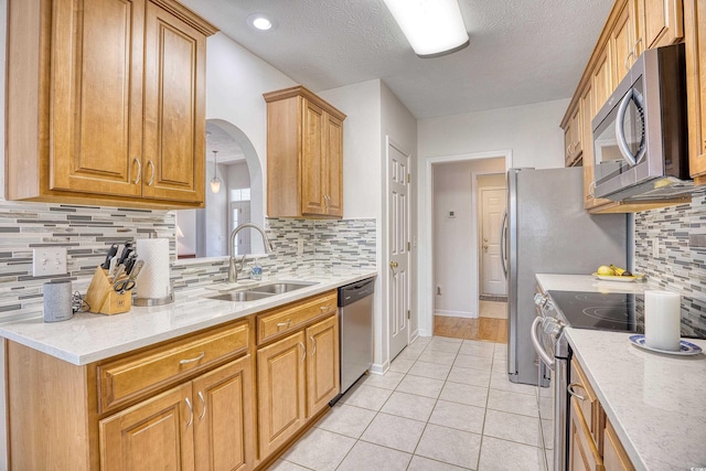 kitchen with light tile patterned floors, arched walkways, a sink, stainless steel appliances, and tasteful backsplash