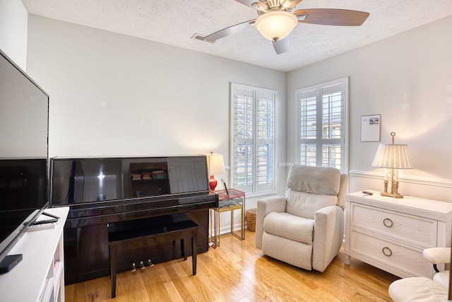 living area featuring a ceiling fan, light wood-style floors, visible vents, and a textured ceiling