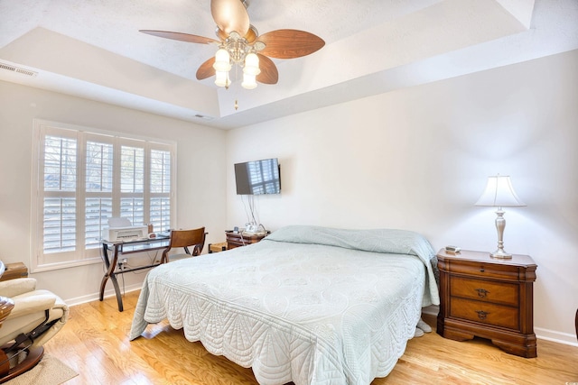 bedroom with a raised ceiling, light wood-style flooring, baseboards, and visible vents