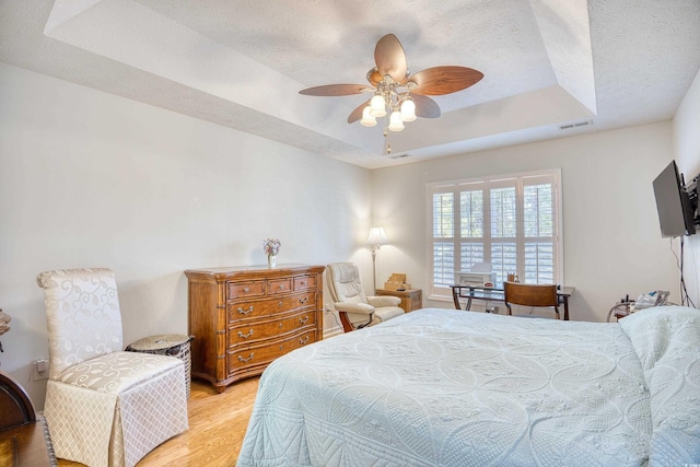 bedroom featuring visible vents, a raised ceiling, a textured ceiling, and light wood-style flooring