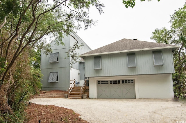 view of front of home featuring an attached garage, dirt driveway, and a shingled roof