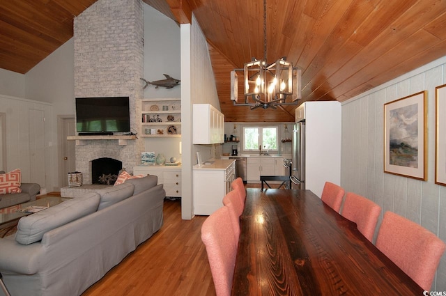 dining room featuring light wood-type flooring, high vaulted ceiling, a notable chandelier, a fireplace, and wood ceiling