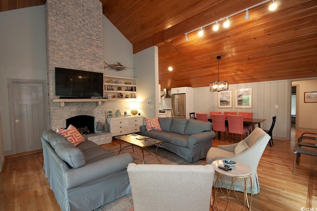 living area with high vaulted ceiling, a fireplace, light wood finished floors, wood ceiling, and a chandelier