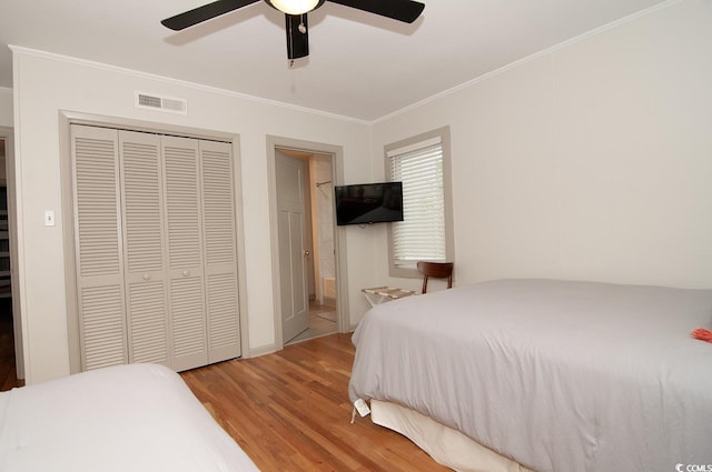 bedroom with a ceiling fan, wood finished floors, visible vents, ornamental molding, and a closet