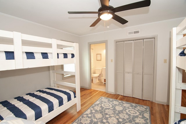 bedroom with visible vents, ornamental molding, wood finished floors, ensuite bath, and a closet