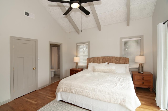 bedroom featuring visible vents, beam ceiling, high vaulted ceiling, wood finished floors, and connected bathroom