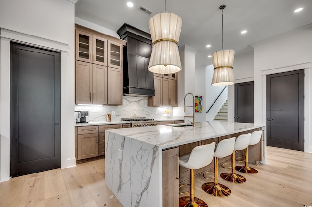 kitchen featuring visible vents, backsplash, a sink, an island with sink, and light wood-type flooring