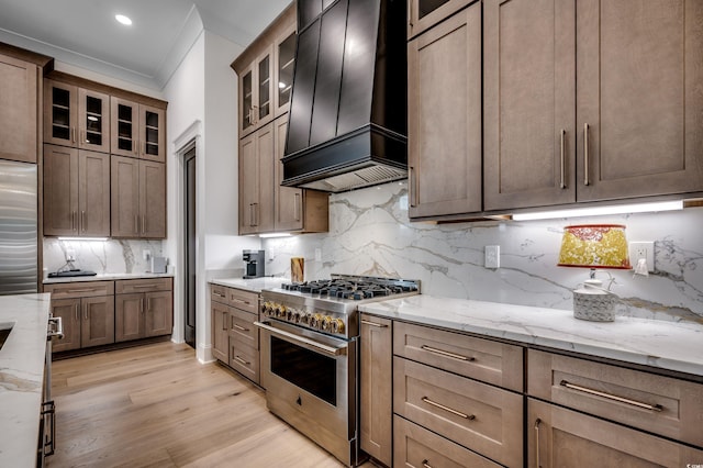 kitchen featuring light stone counters, high end appliances, light wood-style floors, and custom range hood