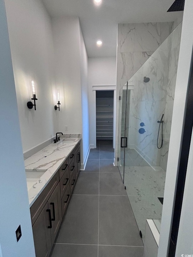 full bath featuring a marble finish shower, double vanity, a spacious closet, a sink, and tile patterned flooring